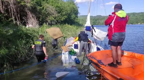 Czterej mężczyźni i pies przy przewróconej żaglówce