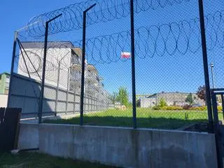 Między ogrodzeniem a najbliższym budynkiem należącym do więzienia jest sporo wolnej przestrzeni 