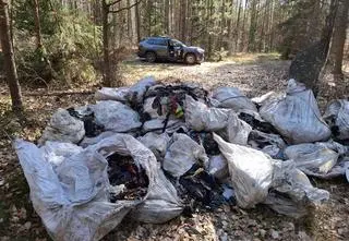 Białe auto i wielkie torby z odzieżą porzucone w lesie