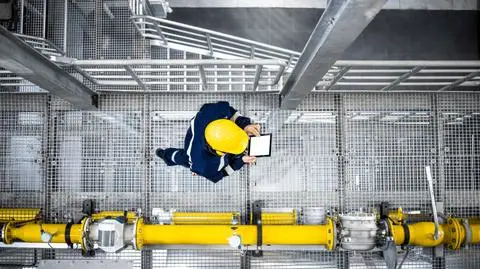 shutterstock_2197733897 Widok z góry na pracownika rafinerii ropy naftowej idącego obok rur gazowych i sprawdzającego produkcję.