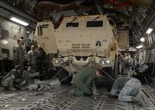Żołnierze mocują wyrzutnię pocisków HIMARS w ładowni ciężkiego samolotu transportowego C-17A