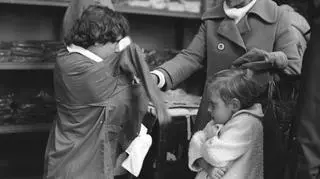 Stoisko z odzieżą szkolną w przejściu między domami towarowymi "Wars" i "Sawa" w Warszawie, Maria Wróblewska mierzy fartuch szkolny, 1977
