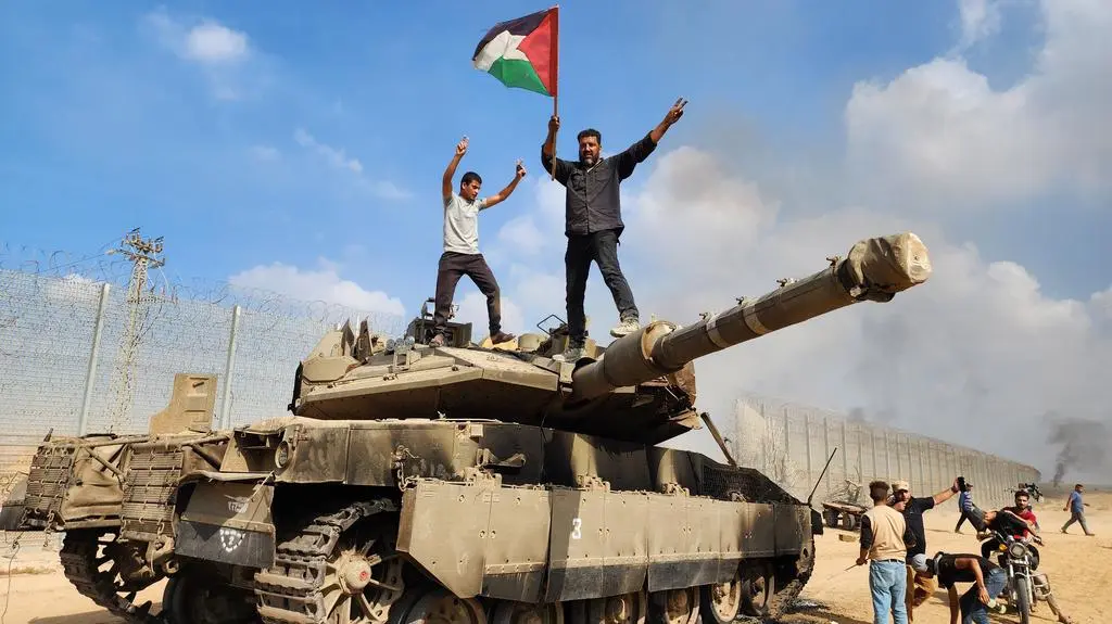 Terroryści Hamasu trzymają palestyńską flagę stojąc na szczycie izraelskiego czołgu. Miasto Gaza, 7 października 2023 r.