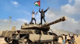 Terroryści Hamasu trzymają palestyńską flagę stojąc na szczycie izraelskiego czołgu. Miasto Gaza, 7 października 2023 r.