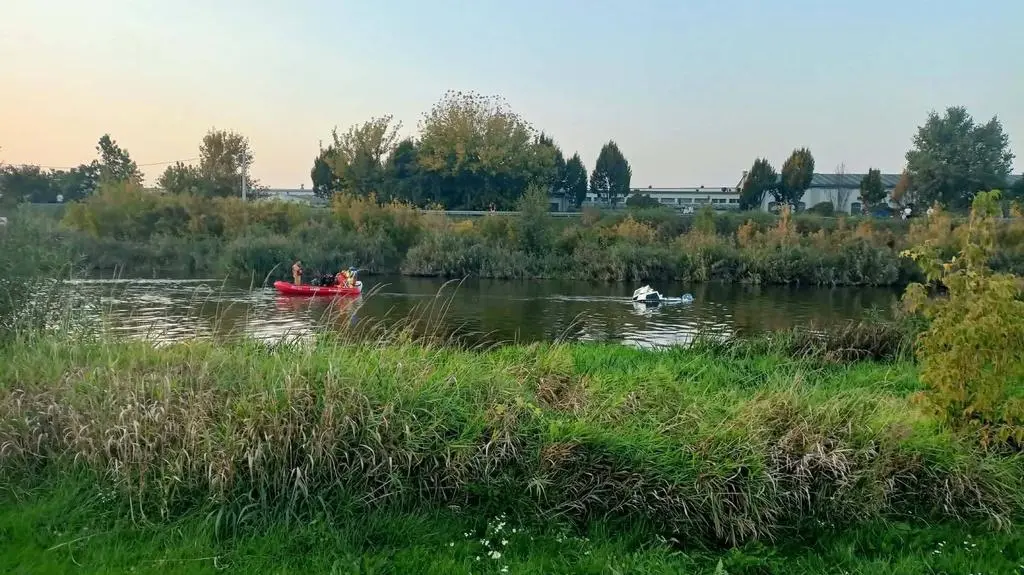 Wywrócona łódź na rzece, obok pijany policjant
