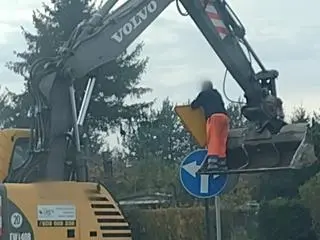 Stał na łyżce od koparki i montował znak