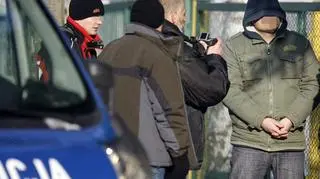 Jeden z podejrzanych prowadzony przez policjantów na miejsce wizji lokalnej w KL Aschwitz (PAP)