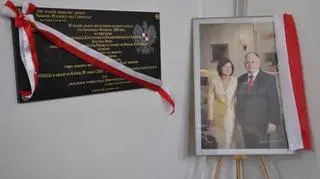 Obok tablicy ustawiono zdjęcie pary prezydenckiej 
