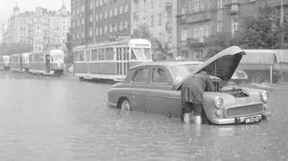 Widok zabudowy po stronie nieparzystej w kierunku placu Unii Lubelskiej. Na pierwszym planie widoczna zepsuta taksówka osobowa marki Warszawa stojąca na środku jezdni z otwartą klapą od silnika. Na dalszym planie widać tramwaje.