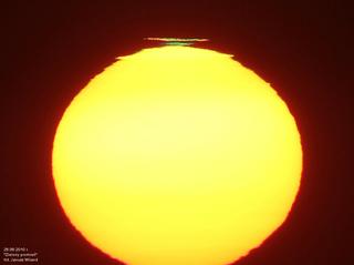 Zielony promień z uwagi na jasność Słońca jest bardzo rzadkim, trudnym i niebezpiecznym zjawiskiem do obserwowania. Osoba niewprawna w obserwacjach tego typu może oślepnąć, bądź zepsuć sobie aparat fotograficzny. Kiedy Słońce jest już blisko horyzontu, a atmosfera nie jest czysta, to blask tarczy Słońca przy horyzoncie jest mniejszy i można spróbować sfilmować lub sfotografować Słońce. Im dłuższa ogniskowa tym lepiej. Do tego filmu zastosowałem ogniskową 120 cm i przesłonę obiektywu lunety, dzięki czemu jasność powierzchniowa zachodzącego Słońca w dniu 26 czerwca 2010 w Piotrkowie Trybunalskim była wystarczająco mała, aby nie zniszczyć mojego aparatu. Z tego zachodu nakręciłem film, który można zobaczyć na YouTube:

http://www.youtube.com/watch?v=VvKsxwKeOoI 

Zdjęcie obok przedstawia kadr z tego filmu z widocznym oderwanym od Słońca jej kawałkiem, który znikając świecił na zielono. Kiedy zobaczymy, że obrzeże zachodzącego Słońca jest poszarpane (nie jest to równy owal) wtedy mamy duże szanse na dostrzeżenie zielonego promienia. 
UWAŻAJCIE, aby nie uszkodzić sobie wzroku, ani aparatu.
